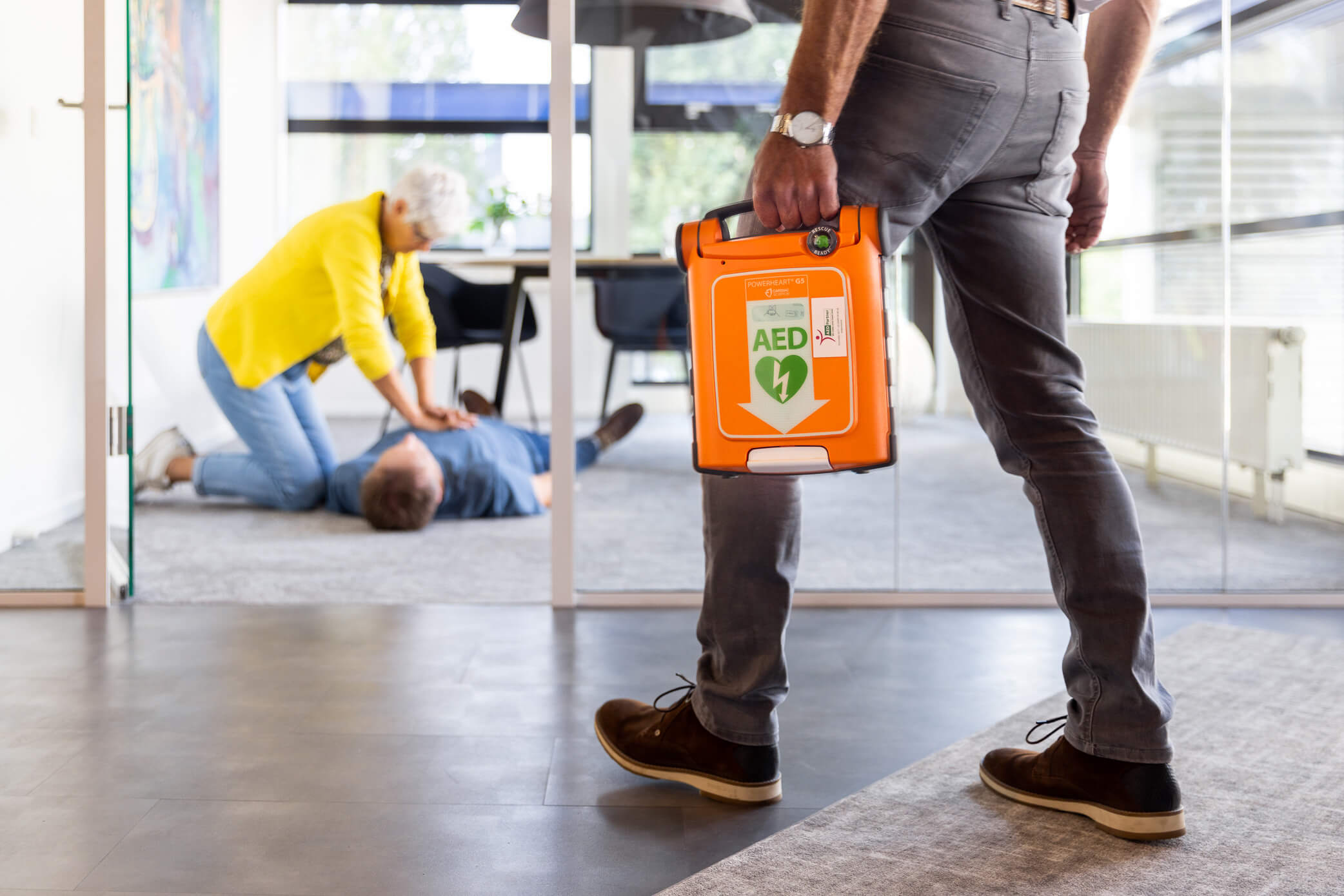 Persoon met Powerheart G5 AED snelt zich naar een reanimatie in een kantoor