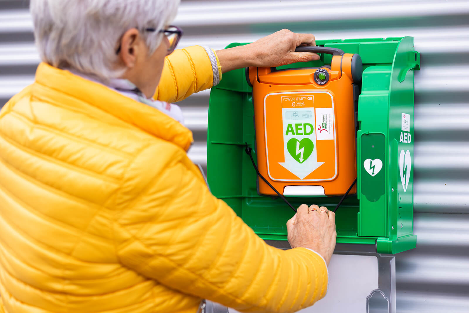 Vrouw pakt een Powerheart G5 AED uit een AED-Kast