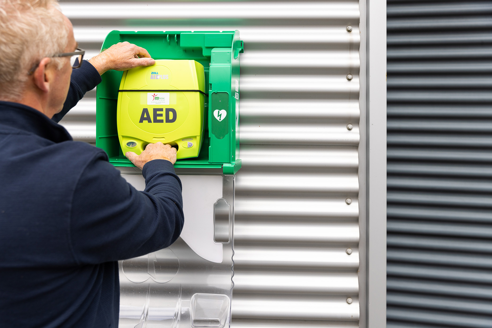 Servicemonteur plaatst een AED in een AED-kast aan de muur.