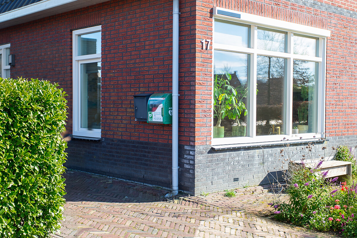 Een AED en bijhorende kast hangen aan een muur van een woning in een nieuwbouwwijk