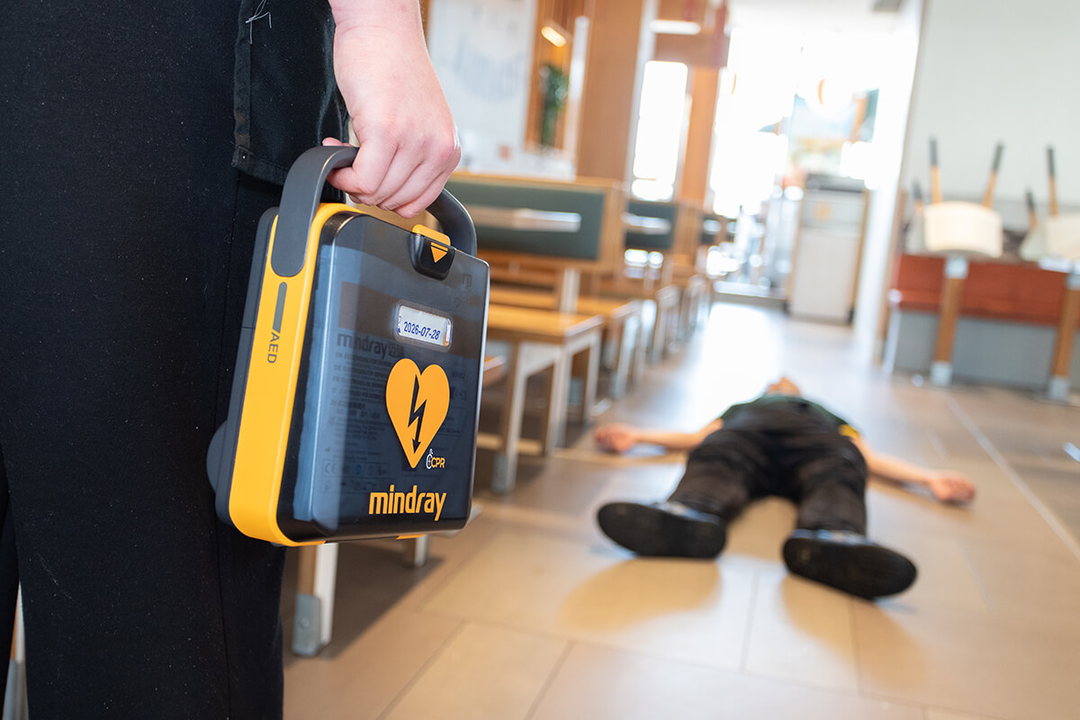 Closeup van aan AED in een restaurant met op de achtergrond een medische situatie