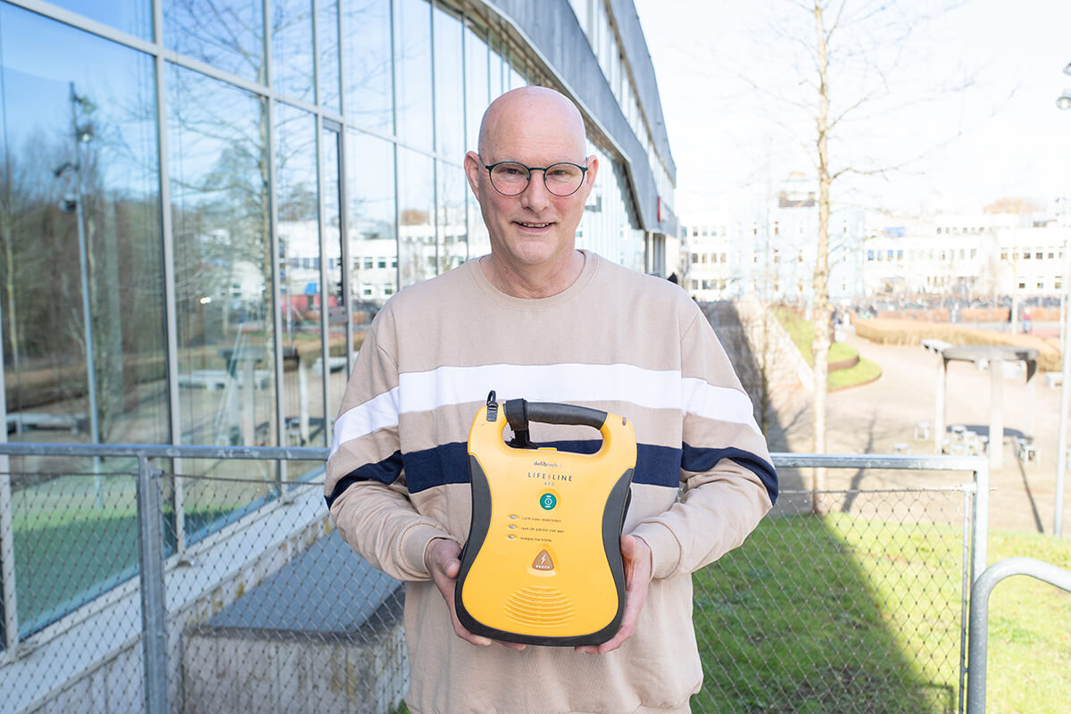 Een medewerker van de gemeente poseert met een AED buiten bij het gemeentehuis
