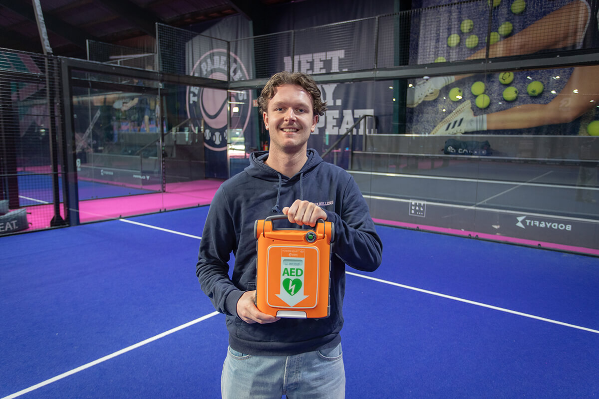 Padelleraar poseert met een AED op de padelbaan