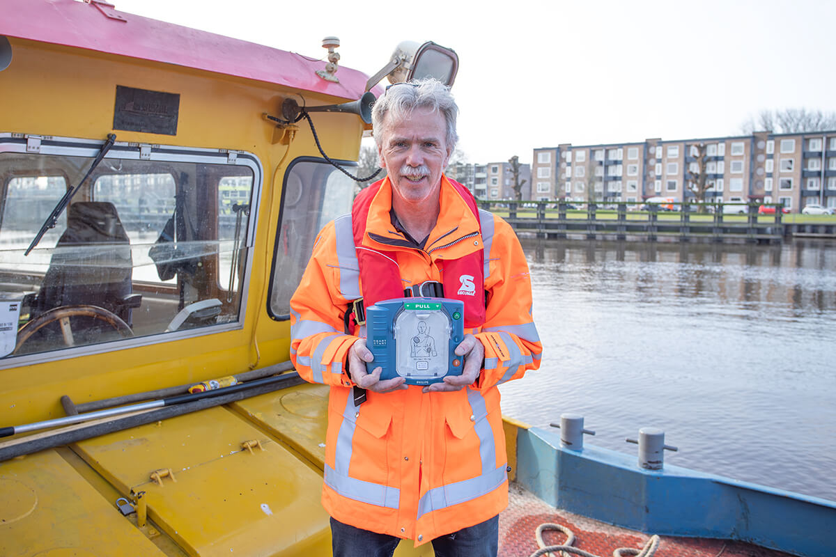 De kapitein van een werkschip poseert met een AED op het dek