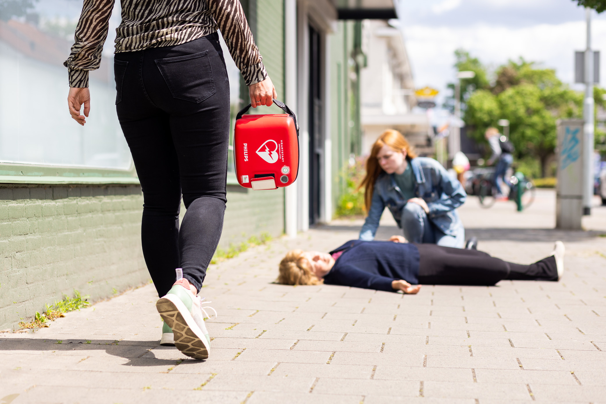Vrouw met AED onderweg naar een medische situatie op de stoep