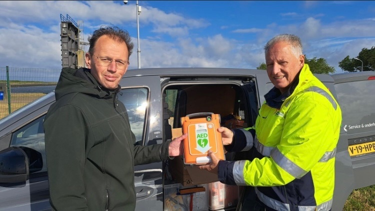 Medewerker AED-Partner en Peter Metske houden samen een AED vast