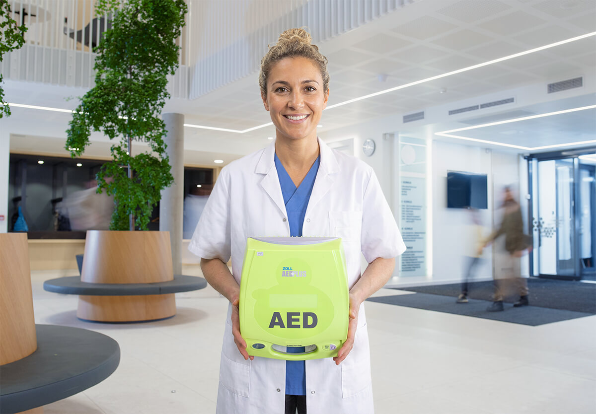 Vrouwelijke arts poseert met AED in de hal van een medisch centrum.