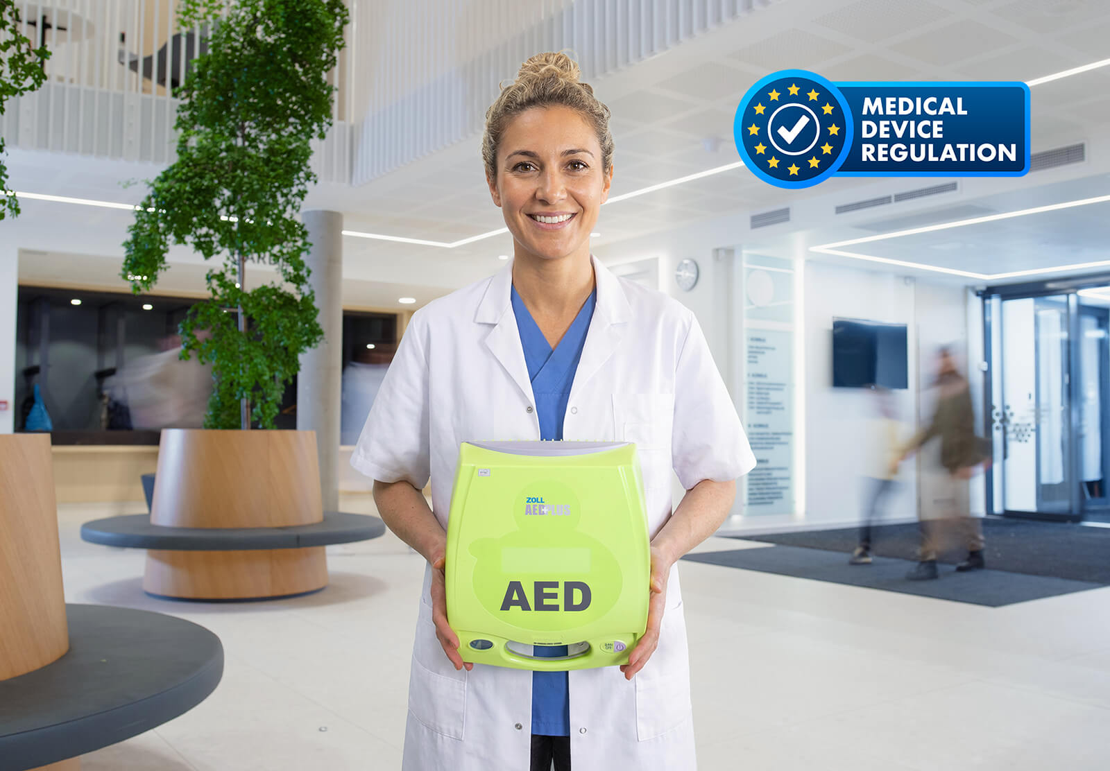 Vrouwelijke arts poseert met AED in de hal van een medisch centrum. MDR vignet staat in beeld